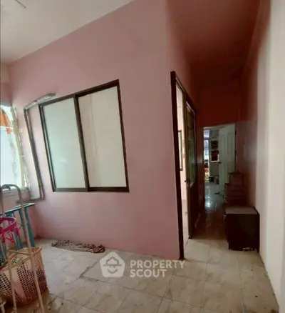 Cozy interior space with pink walls and tiled flooring, featuring a window and hallway.