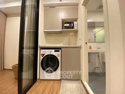 Modern compact kitchen with washing machine and microwave, adjacent to a sleek bathroom.