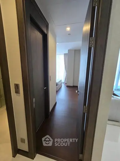 Modern apartment hallway with wooden flooring leading to a bright living area with large windows.