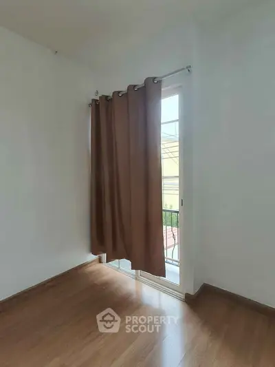 Bright room with wooden flooring and large window with brown curtains, perfect for cozy living.