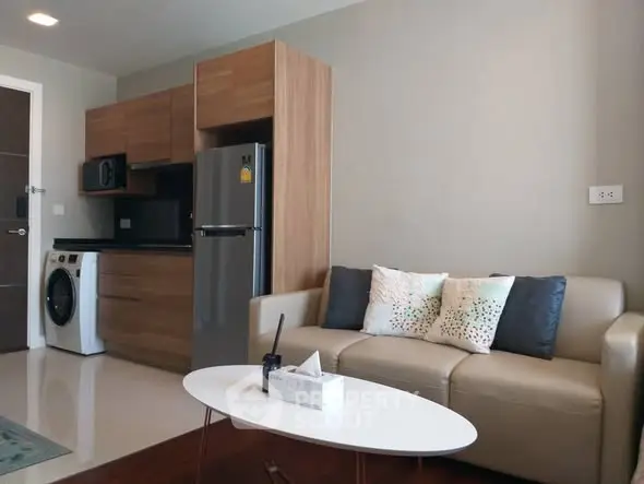 Modern living room with sleek kitchen, featuring stainless steel appliances and cozy seating area.