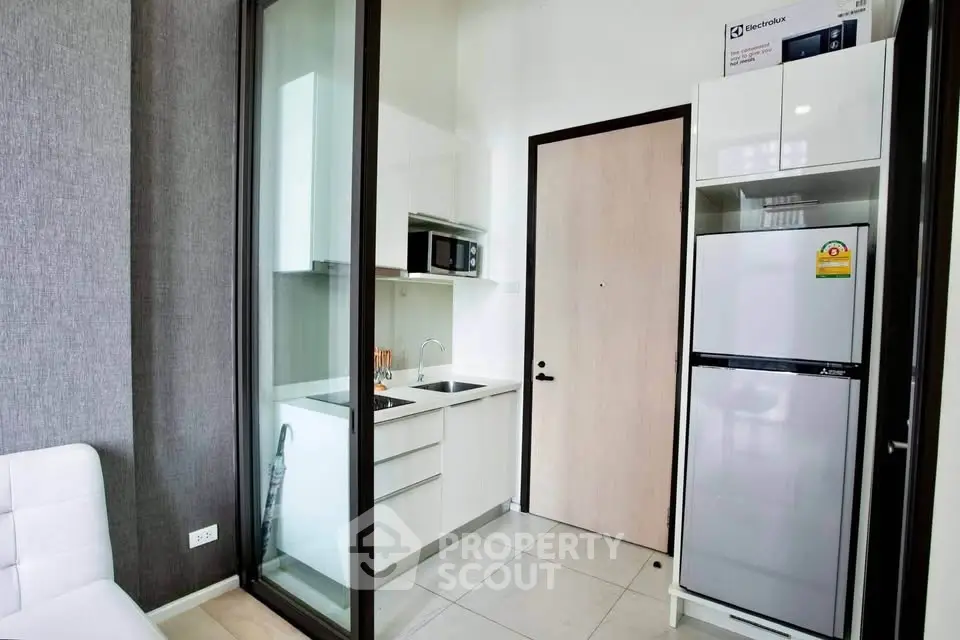 Modern compact kitchen with sleek appliances and glass partition in stylish apartment.
