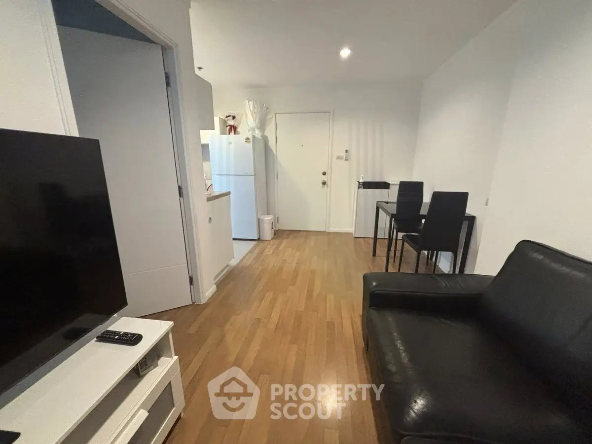 Modern living room with sleek black leather sofa, wooden flooring, and open kitchen layout.