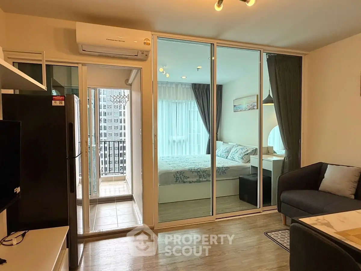 Modern apartment with glass-walled bedroom and cozy living area, featuring a small balcony with city view.