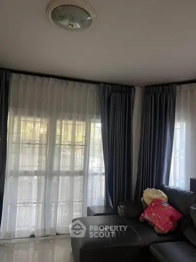Cozy living room with large windows and elegant curtains, featuring a comfortable leather sofa.