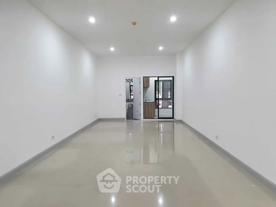 Spacious unfurnished living room with glossy tiled floors and bright lighting, leading to a modern kitchen.