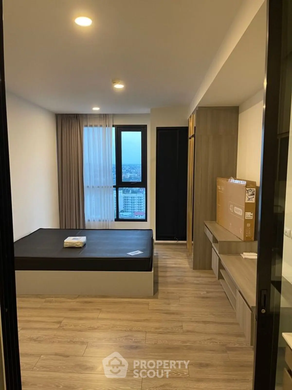 Modern bedroom with large window and wooden flooring in high-rise apartment