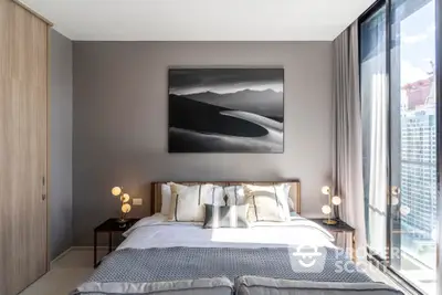 Modern bedroom with large bed, elegant bedding, and stylish wall art, complemented by ambient lighting and a city view through floor-to-ceiling windows.