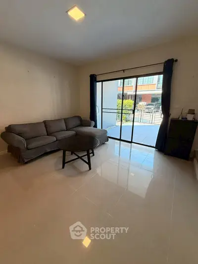 Spacious living room with modern sofa and large window offering natural light and outdoor view.