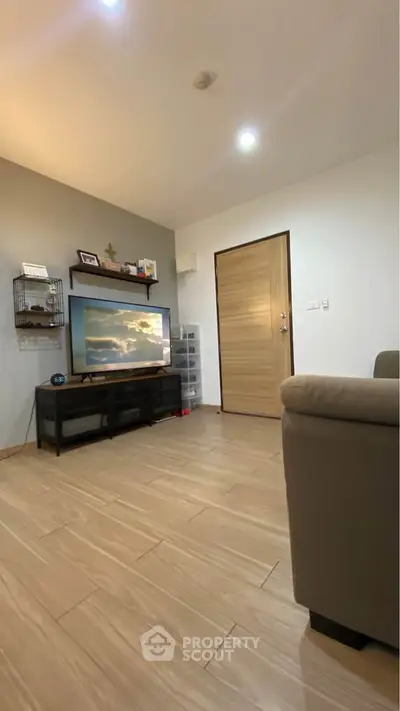 Modern living room with wooden flooring and stylish decor, featuring a flat-screen TV and cozy seating.