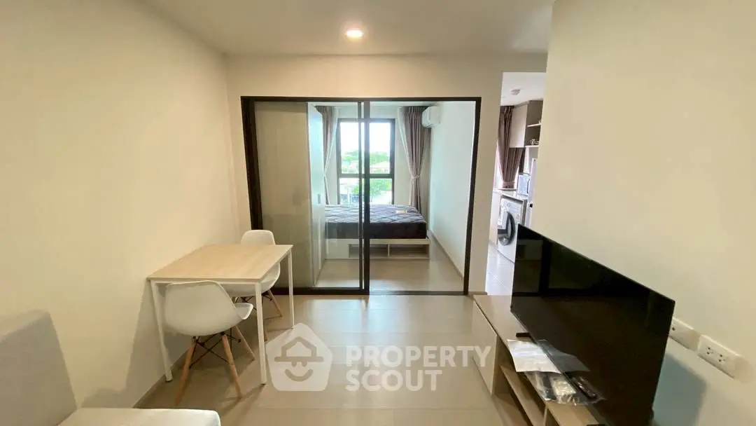 Modern apartment interior with open living room and bedroom view, featuring sleek furniture and natural light.