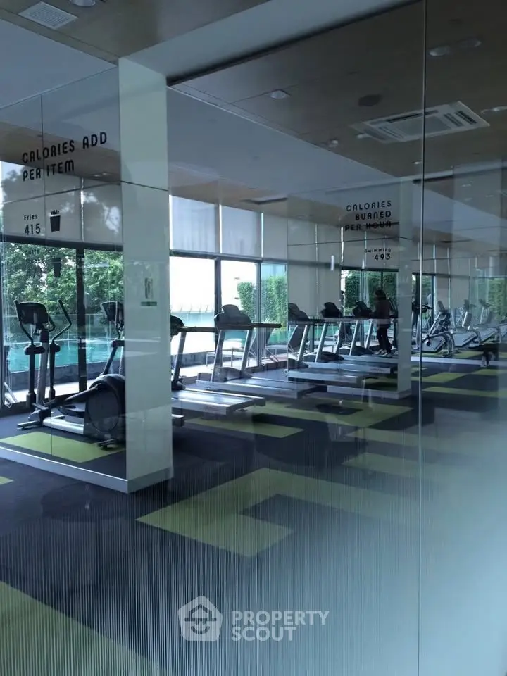 Modern gym with cardio equipment and large windows overlooking greenery.