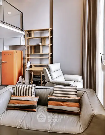 Modern loft-style living room with stylish furniture and vibrant orange fridge