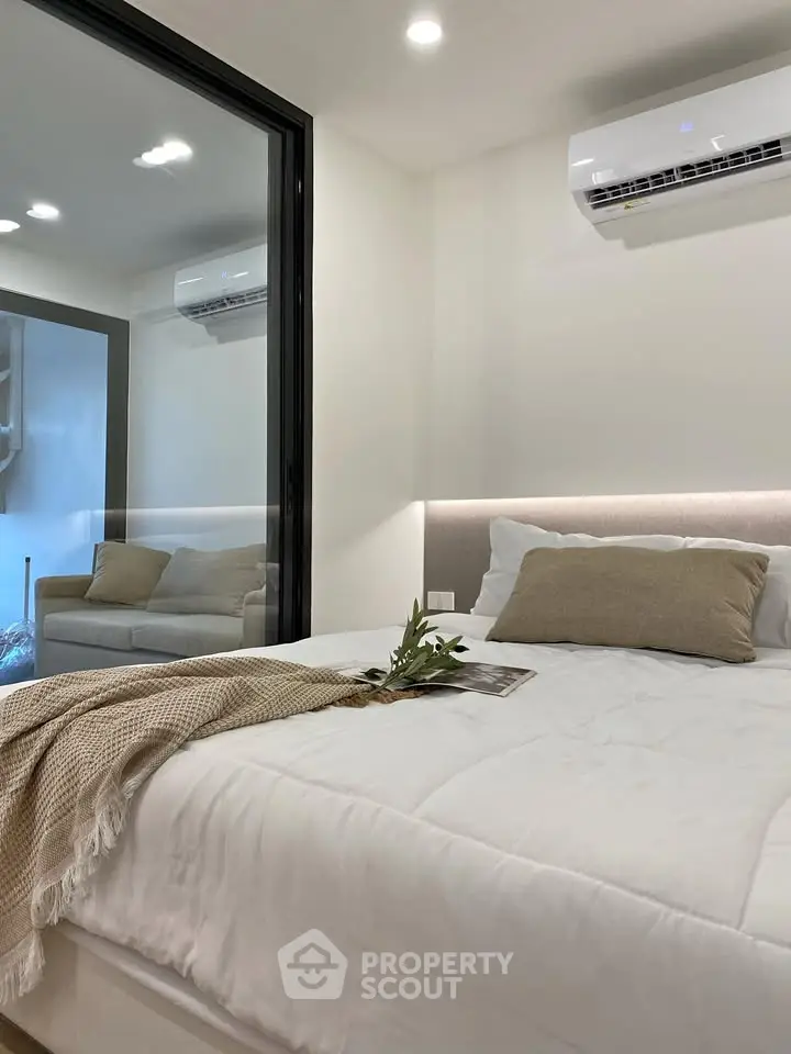 Modern bedroom with cozy bed and air conditioning, featuring a glass partition and neutral decor.