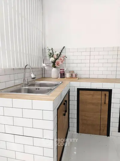 Modern kitchen with sleek white tiles and wooden cabinets, featuring a stainless steel sink and elegant decor.