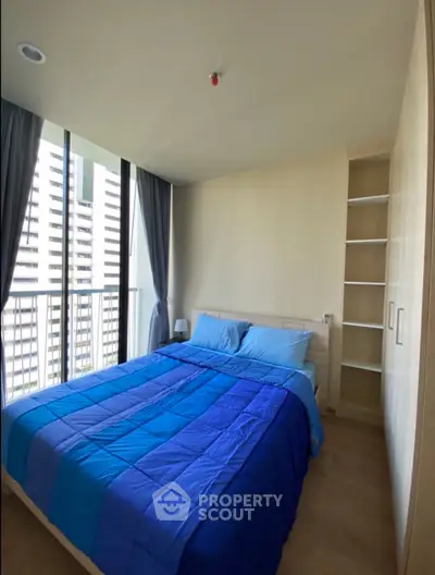 Modern bedroom with large windows and blue bedding in a high-rise apartment.