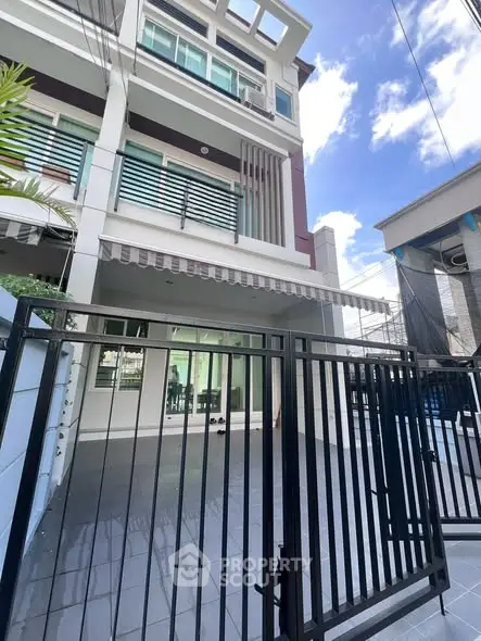 Modern multi-story townhouse with gated entrance and spacious balcony under a clear blue sky.
