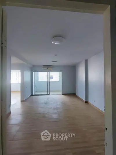 Spacious empty living room with wooden flooring and large windows for natural light.