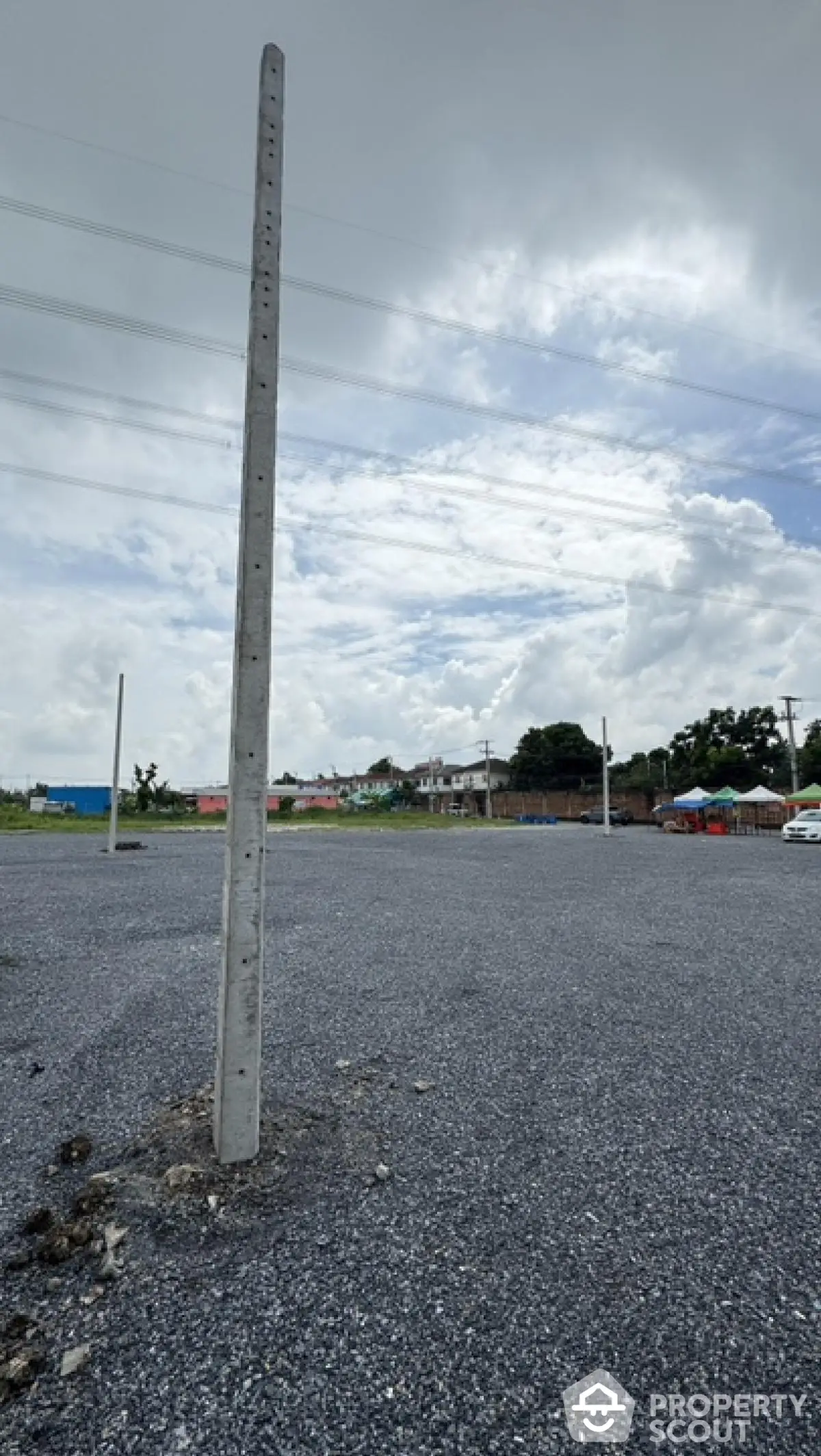 Spacious gravel parking lot with utility poles under a cloudy sky