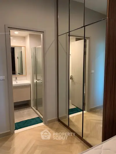 Modern bedroom with mirrored closet doors and en-suite bathroom in stylish apartment.