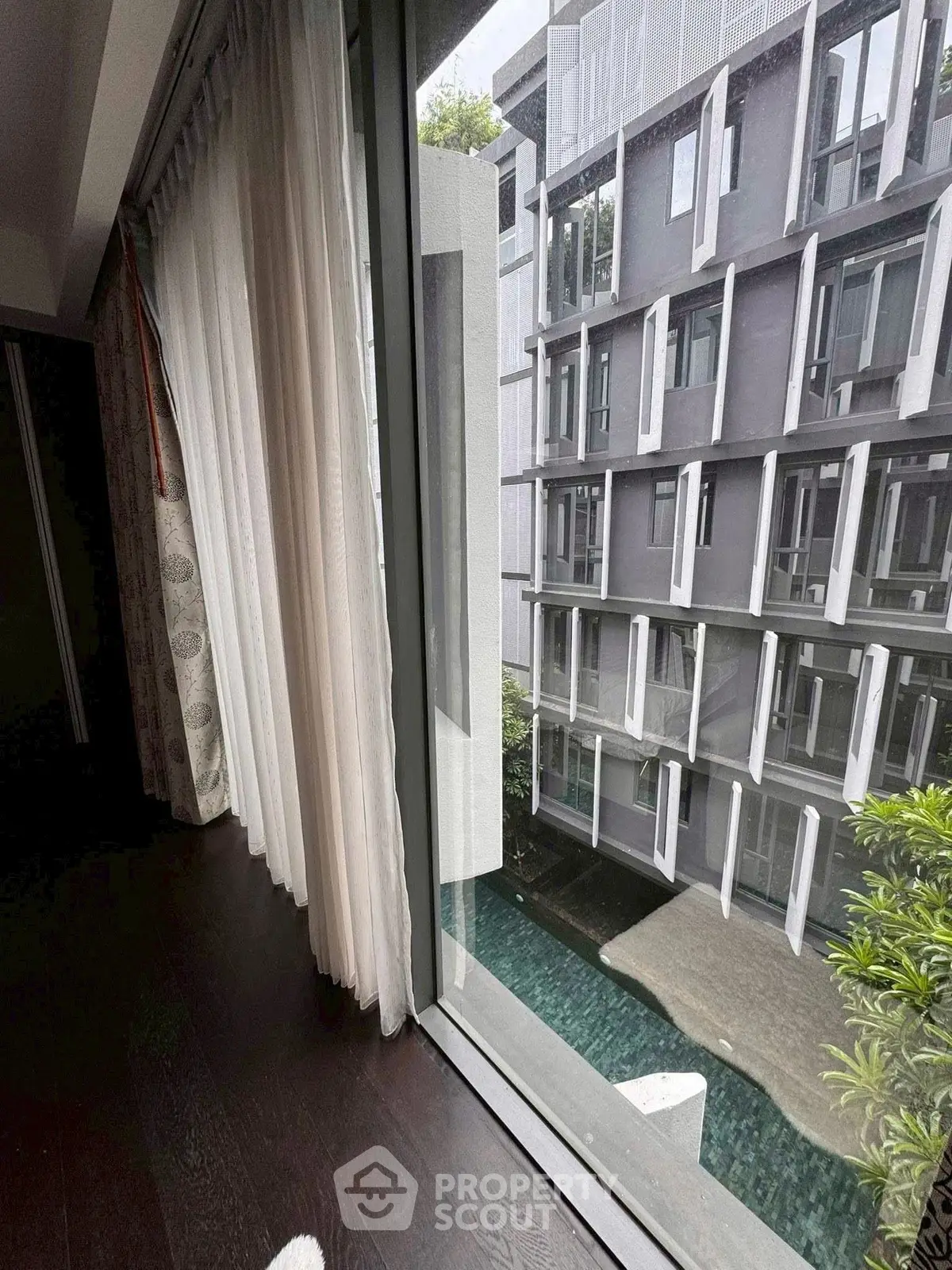 Modern apartment view with floor-to-ceiling windows overlooking a stylish building and pool area.