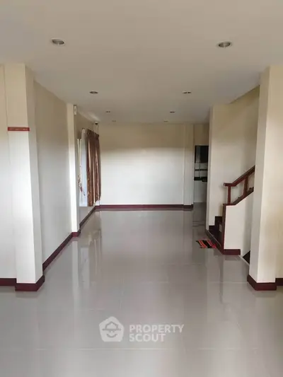 Spacious empty living room with glossy tiled floors and staircase, ready for customization.