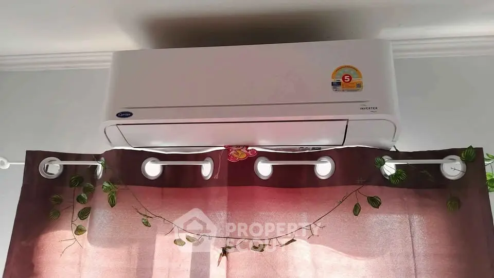 Modern air conditioning unit installed above window with decorative curtains and greenery.