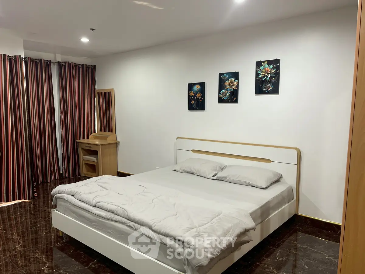 Spacious bedroom with modern decor and elegant artwork, featuring a comfortable bed and stylish curtains.
