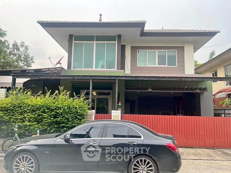Modern two-story house with large windows and red fence, featuring a sleek black car parked in front.