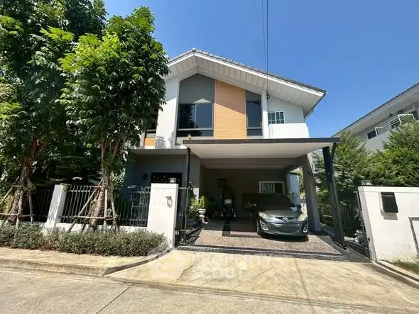 Charming two-story house with carport and lush greenery in a serene neighborhood.