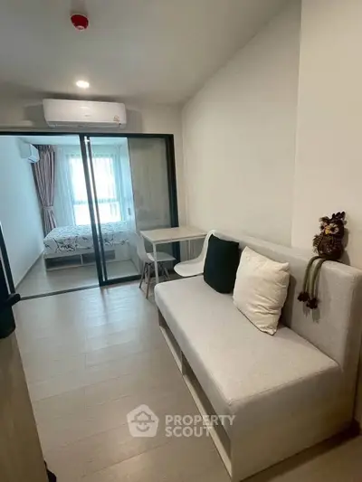 Modern apartment interior with cozy living area and sliding glass doors leading to a bright bedroom.