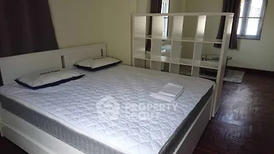 Spacious bedroom with modern white bed and partition, hardwood floors, and natural light.