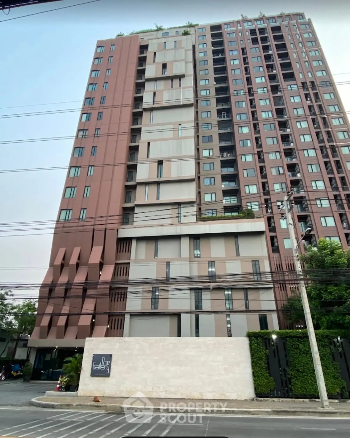 Modern high-rise building exterior with unique architectural design and lush greenery at entrance.