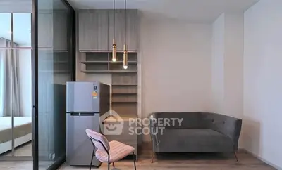 Modern apartment interior with stylish sofa, chair, and fridge in open layout.