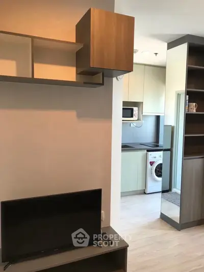 Modern apartment interior with compact kitchen and living area featuring washing machine and TV.