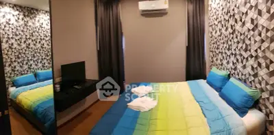 Modern bedroom with geometric wallpaper and vibrant bedding in a stylish apartment.