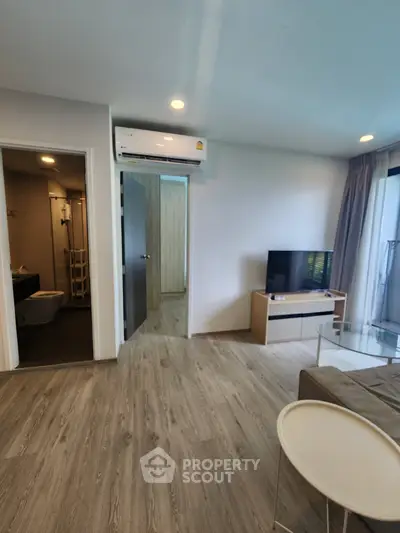 Modern living room with wooden flooring, TV, and air conditioning, adjacent to bathroom and bedroom.
