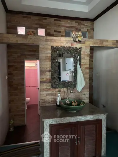 Charming bathroom with unique stone wall and decorative mirror, featuring a stylish floral basin and wooden cabinet.