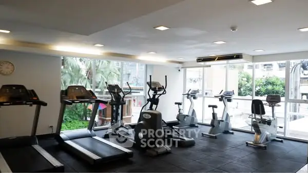 Modern gym with cardio equipment and large windows in a residential building.