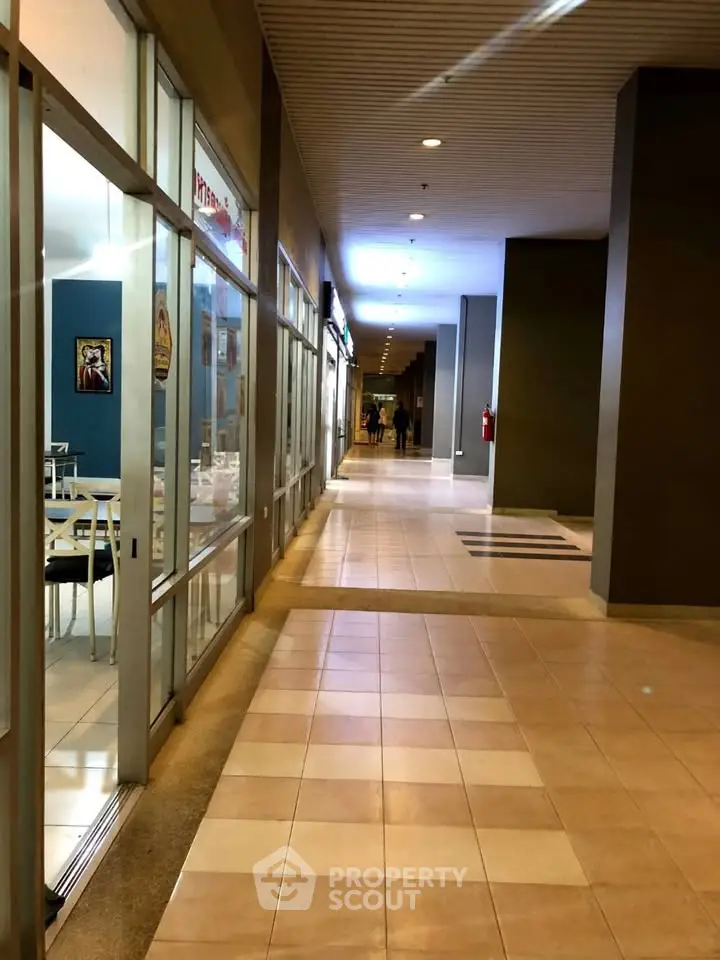 Spacious commercial corridor with modern tile flooring and glass storefronts