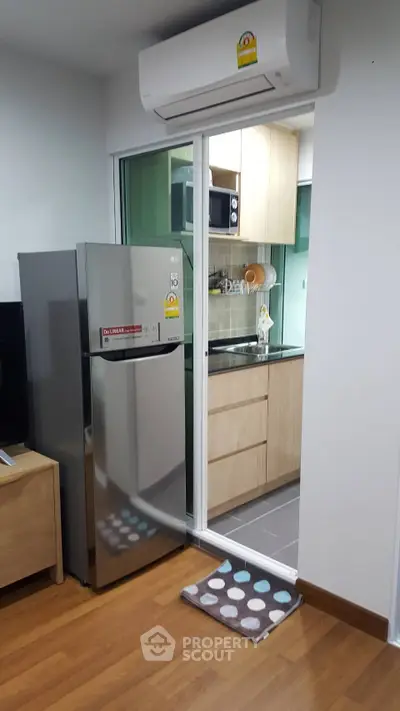 Modern compact kitchen with stainless steel fridge and microwave in cozy apartment.