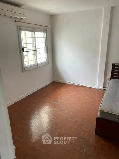 Spacious bedroom with wooden flooring and natural light from window.