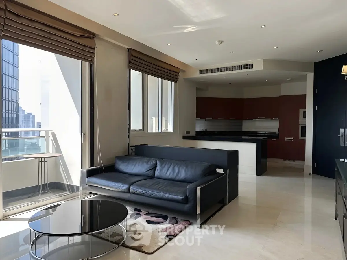 Modern living room with sleek black sofa and open kitchen in high-rise apartment with city view.