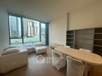 Spacious modern living room with large windows and city view, featuring elegant furniture and shelving.