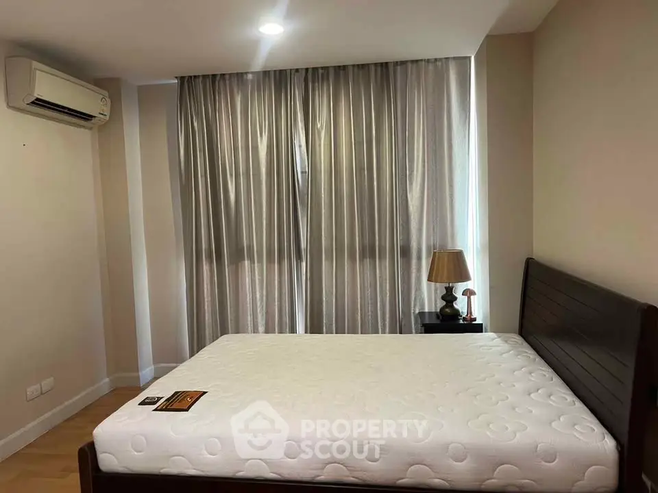 Cozy bedroom with large window and elegant curtains, featuring a comfortable bed and stylish lamp.