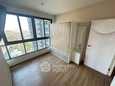 Spacious bedroom with large window offering stunning city views in modern apartment.