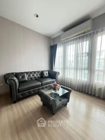 Stylish living room with elegant black leather sofa and glass coffee table, featuring large windows and natural light.