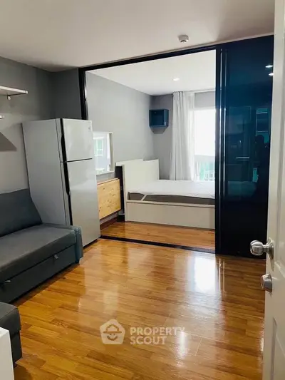 Modern studio apartment with sleek design, featuring a cozy living area and a compact kitchen with a large fridge.