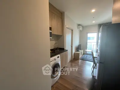 Modern apartment interior with open kitchen and living area, featuring a washing machine and sleek wooden flooring.