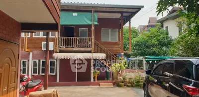 Charming two-story wooden house with outdoor staircase and lush greenery, perfect for serene living.